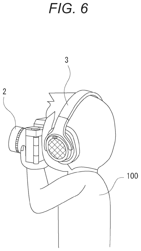 A person wearing a headset and holding a camera, demonstrating how the camera can be controlled by headset gestures. Drawing from patent filing US 2026/0299702 A1.